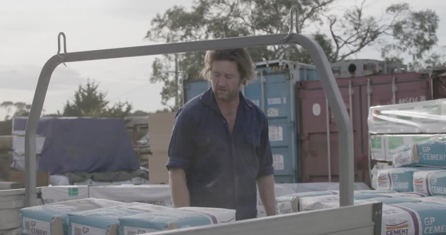 A man is putting large bags of concrete in the back of his truck