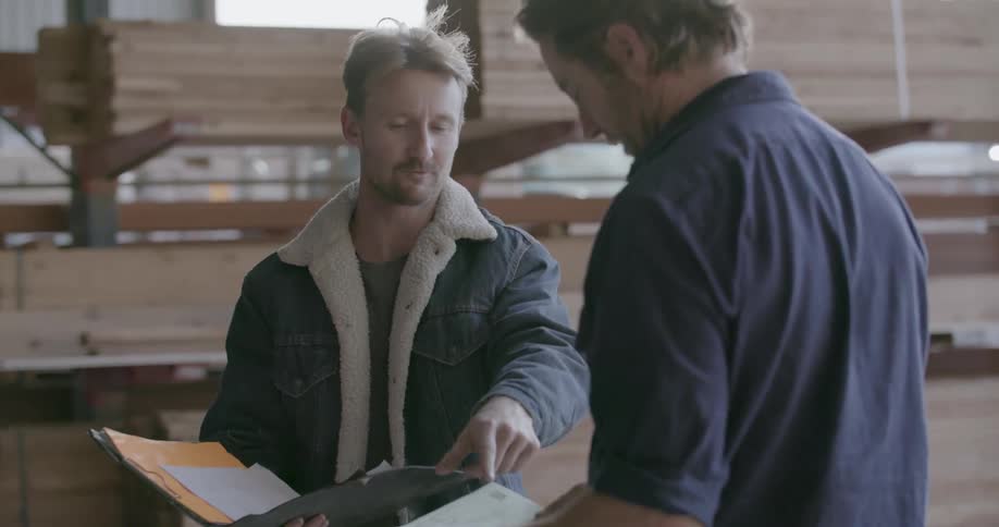 Two men are talking business in lumber warehouse during the day