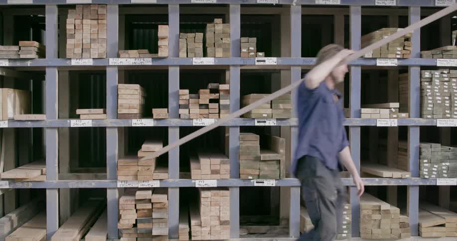Man carrying a plank of wood as he passes shelves full of them