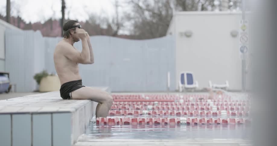 A man is splashing himself and putting on goggles before going for a swim