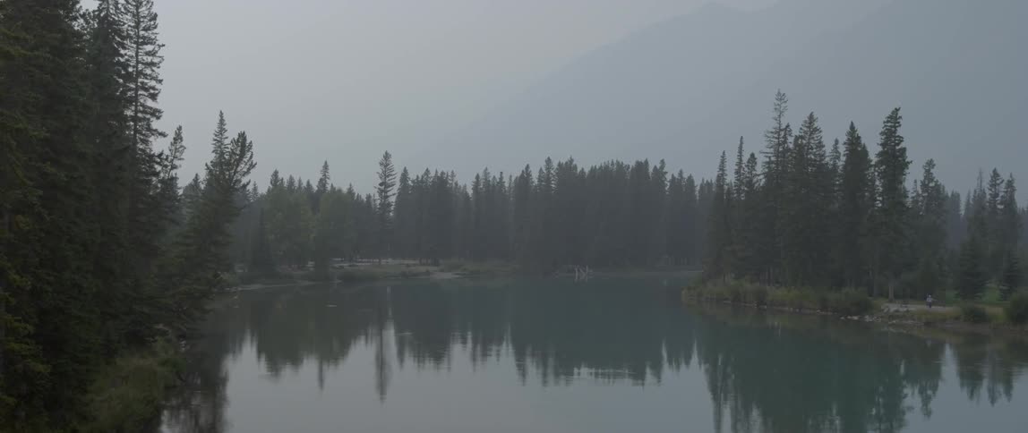 Fog is lingering over a forest lake and mountains at dawn