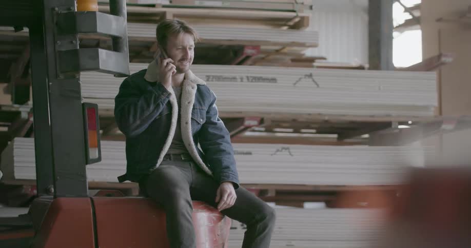 A man is talking on a cellphone while working in a lumberyard during the day