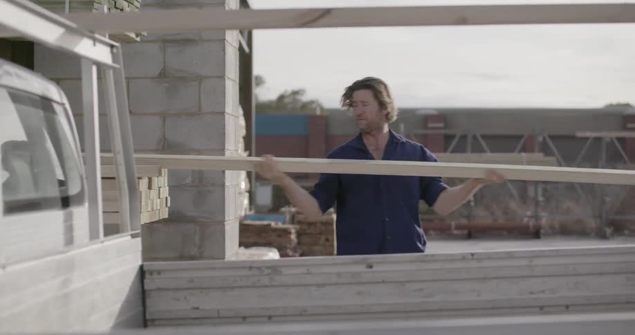 A man is taking pieces of lumber and putting it on his truck