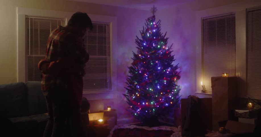 A man and woman hug next to a christmas tree