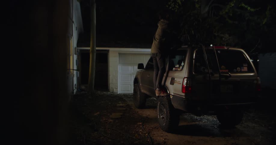 Man arriving home and removing a christmas tree from the top of his vehicle at night