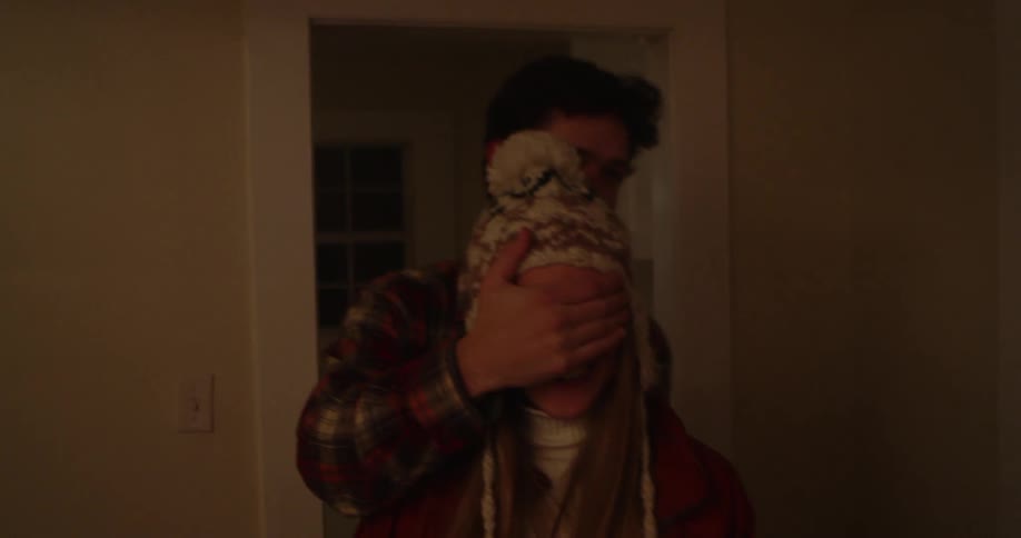 A man covers a woman's eyes playfully as they walk through a house