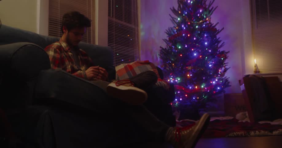 A man sits on a couch by a lit christmas tree