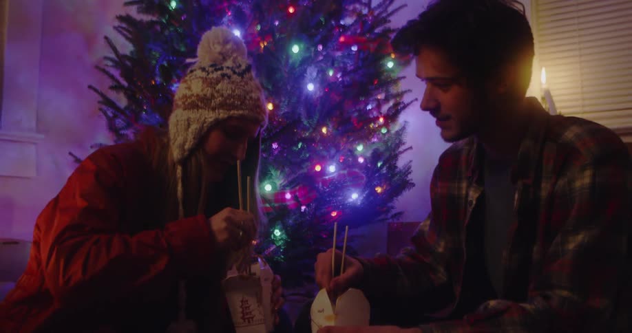 A man and woman eat chinese food by the christmas tree