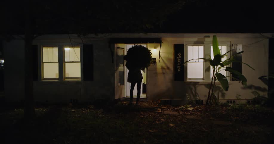 A man carries a christmas tree through the front door of a house