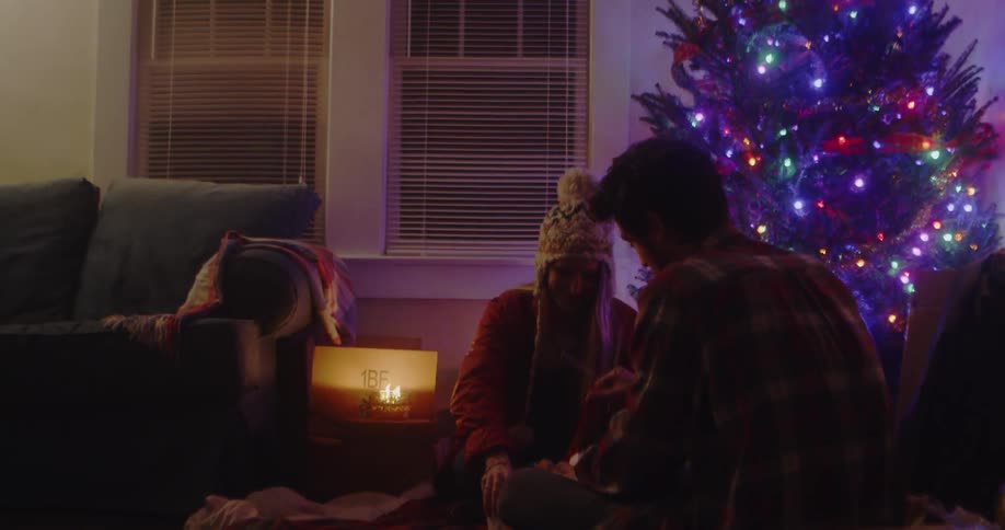 Man and woman sit in candle light next to a lit up christmas tree