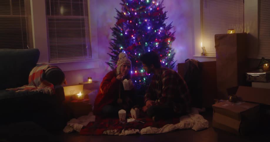 A man and woman eat chinese food by the christmas tree