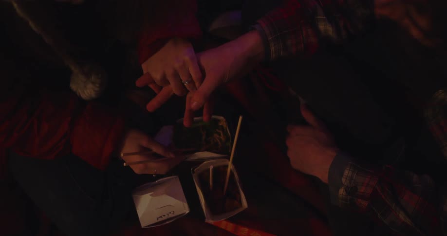 A man and woman are holding hands as they share chinese food inside at night