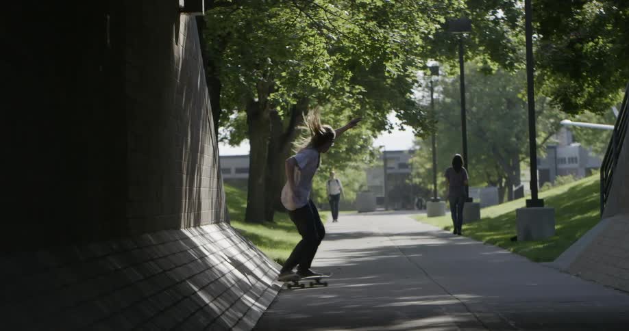 Man skateboards down a sidewalk and does a jump off the wall
