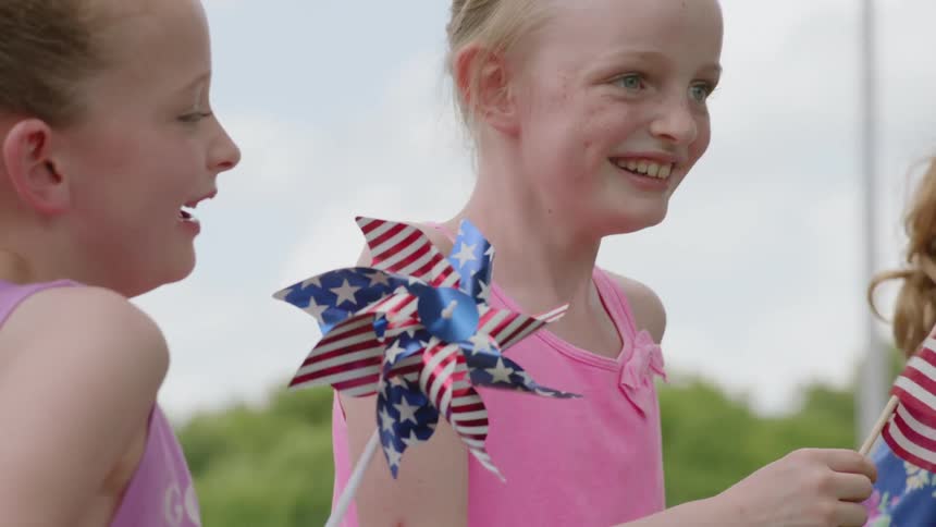 Girls smile as they wave flags and pinwheels