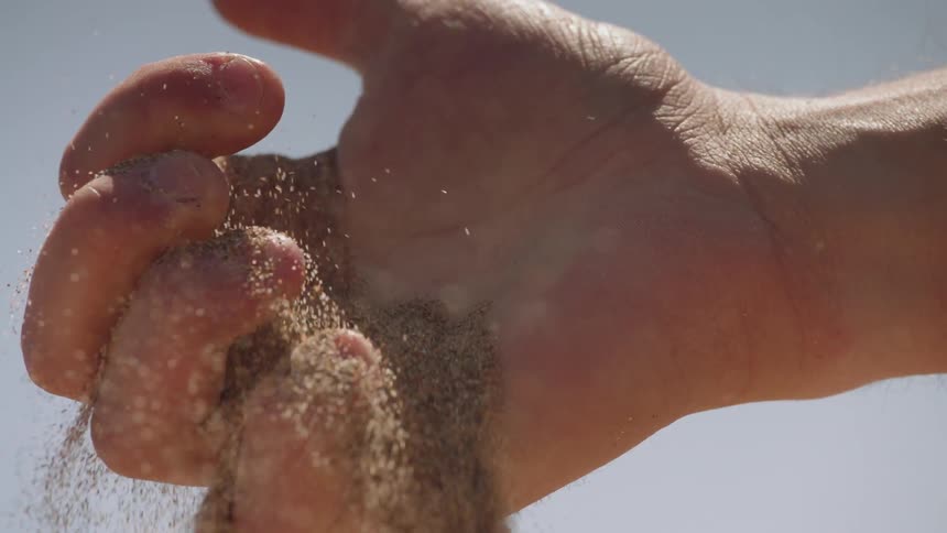 Small particles flowing form a fist as it releases them on a clear day