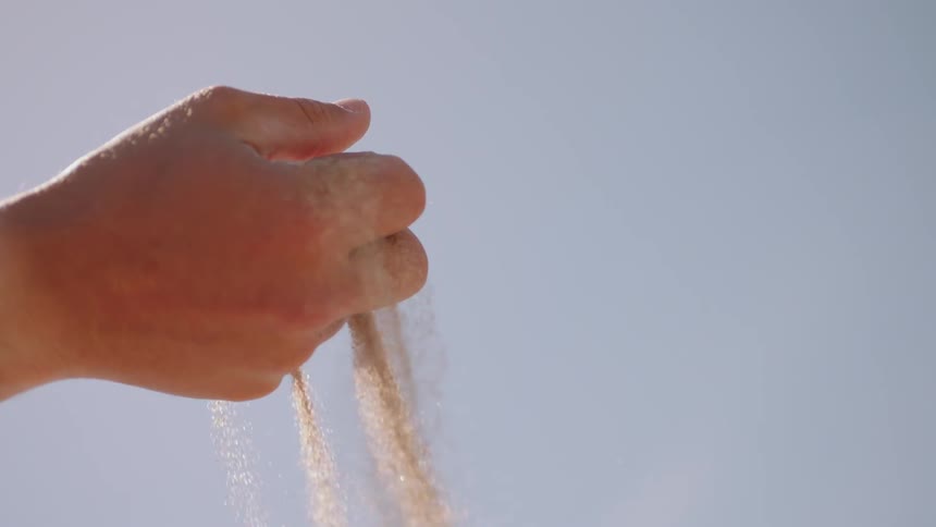 Sand filters through a person's hand in the desert