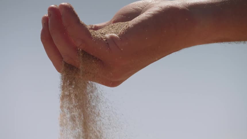 A man holding dirt in his hand slowly has it fall out