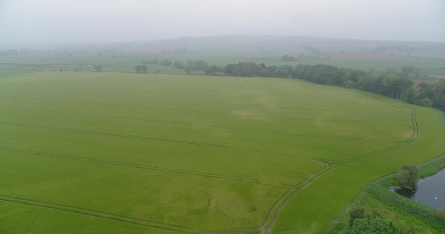 Fog is lingering in the air above farm fields and a river during the day