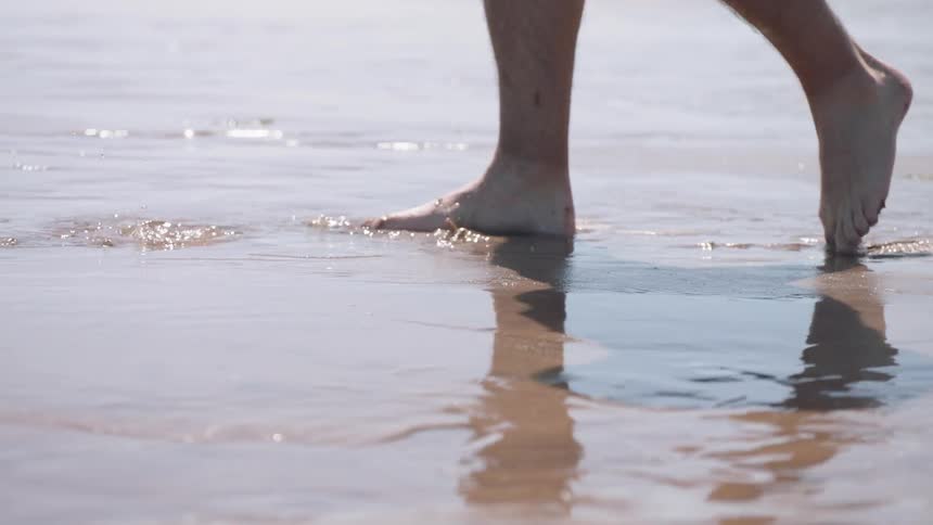 Person's feet steps into shallow water and mud