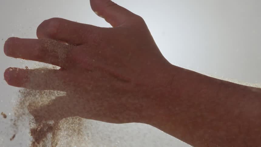 A man opens his hand and lets the sand fly and fall out