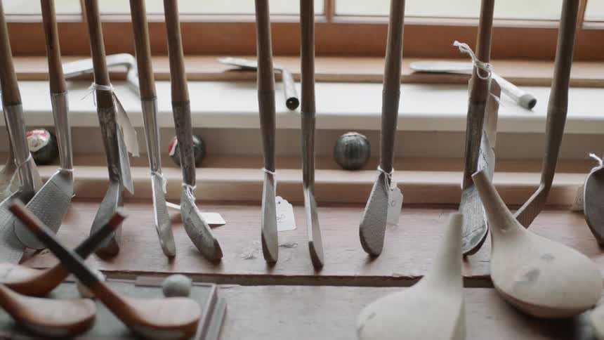 Golf clubs with price tags line a rack near a window