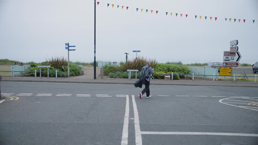 Man walking while carrying his golf clubs down a street on an overcast day