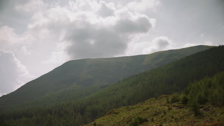 Sun partially blocked by clouds over grassy hills
