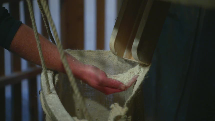A man is catching ground grain in his hand as it falls from a chute