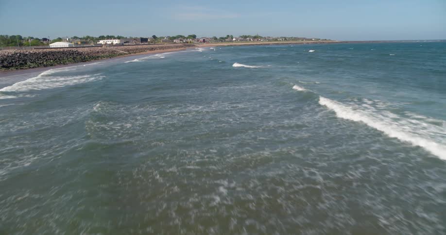 Waves are rolling towards a beach in a coastal community on a sunny day
