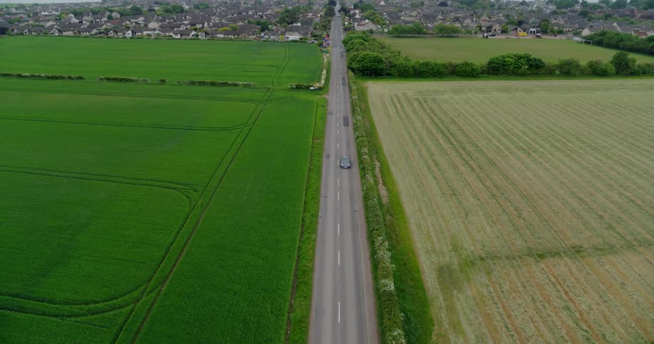 A vehicle travels down a road next to farm crops