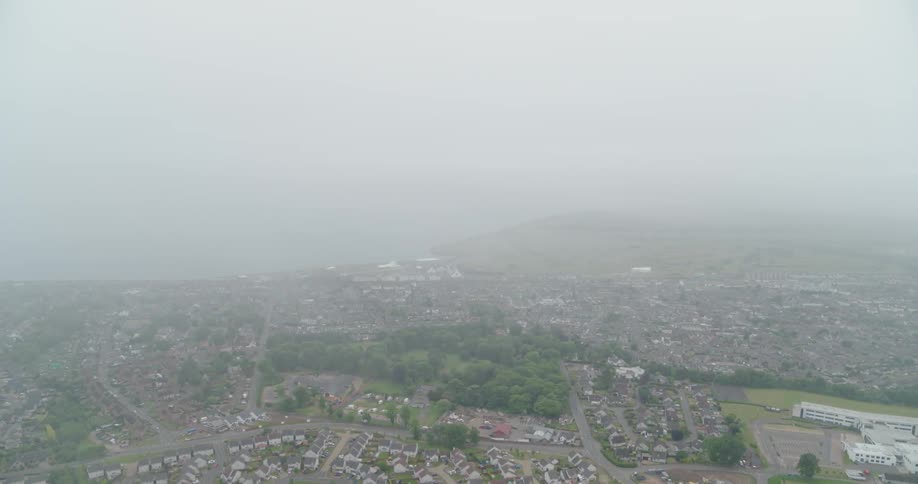 Fog and clouds are drifting over a coastal community during the day