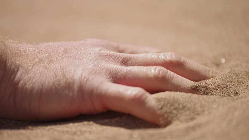 A man sinks his hand into the sand