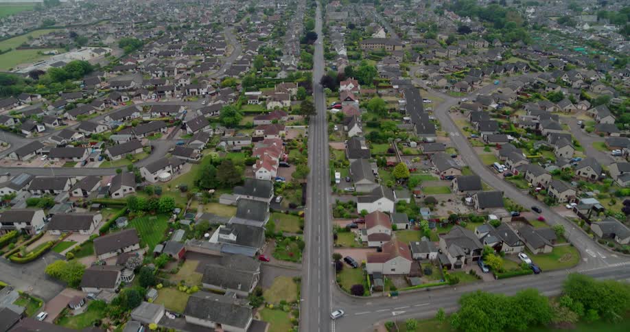 Vehicles are driving on a road into a town on a cloudy day