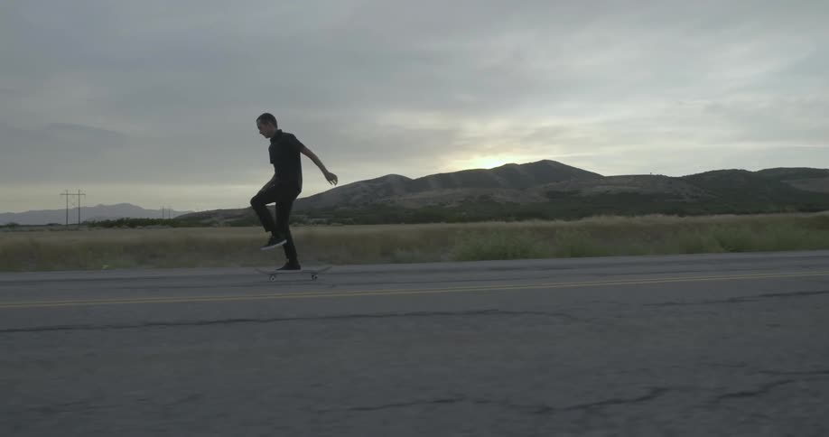 Man riding his skateboard on a cloudy day down a road