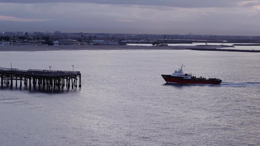 A ship floats by a pier at sunset