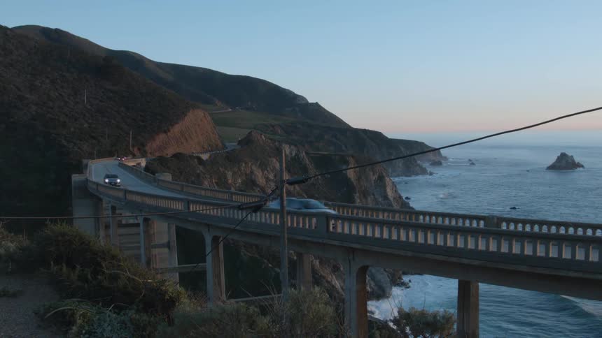 Cars drive on a bridge over the water at sunrise