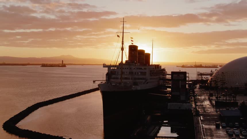 A seagull is flying in the sky above a commercial vessel at sunset