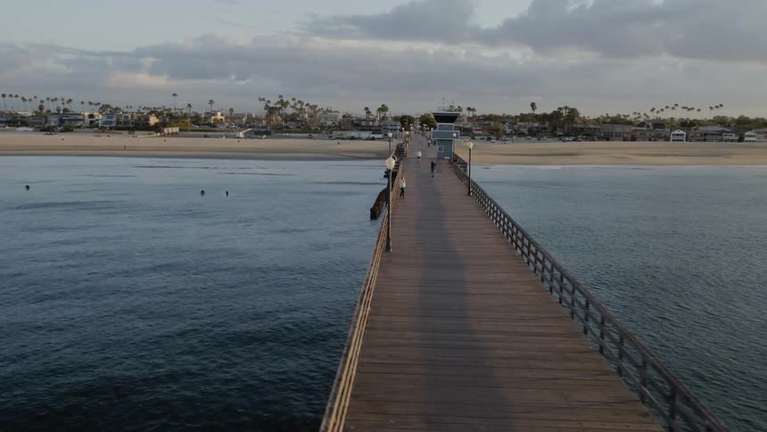 People are walking on a pier on the coast at dusk