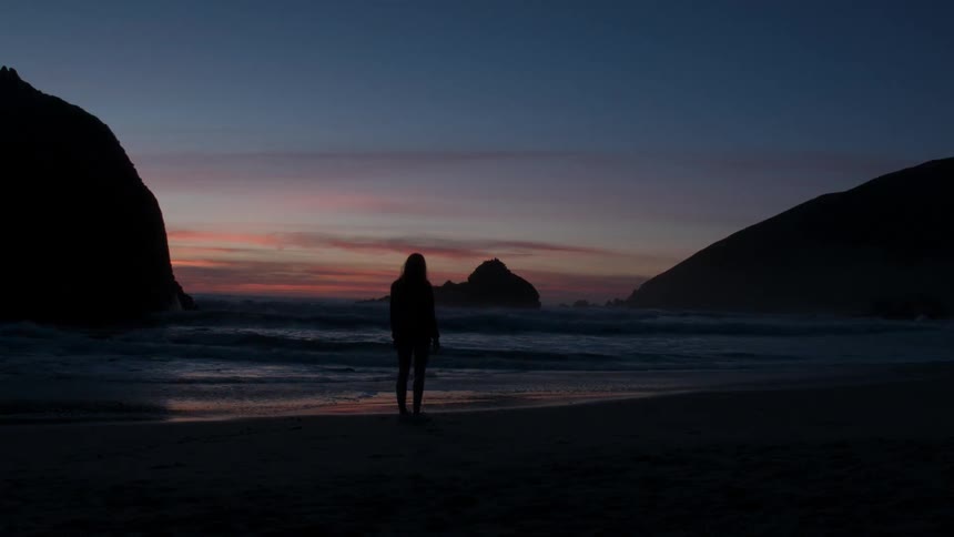 A woman stands on a beach at dusk
