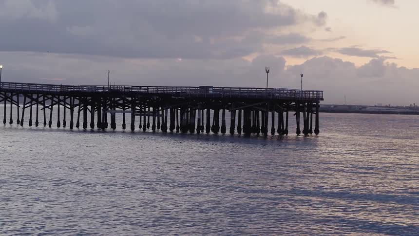 The ocean tide is rolling beneath a pier on the coast at dusk