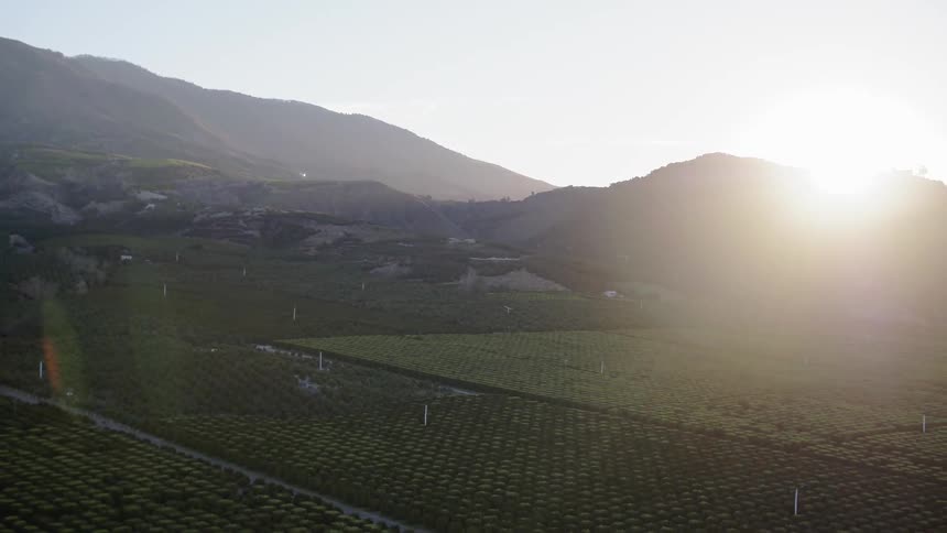 The sun rising behind some mountains over farmland