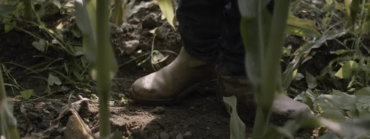A man in gardening boots steps in the muddy dirt