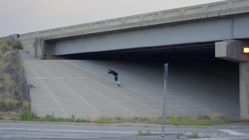 A young man skateboards down a bridge ramp on an overcast day