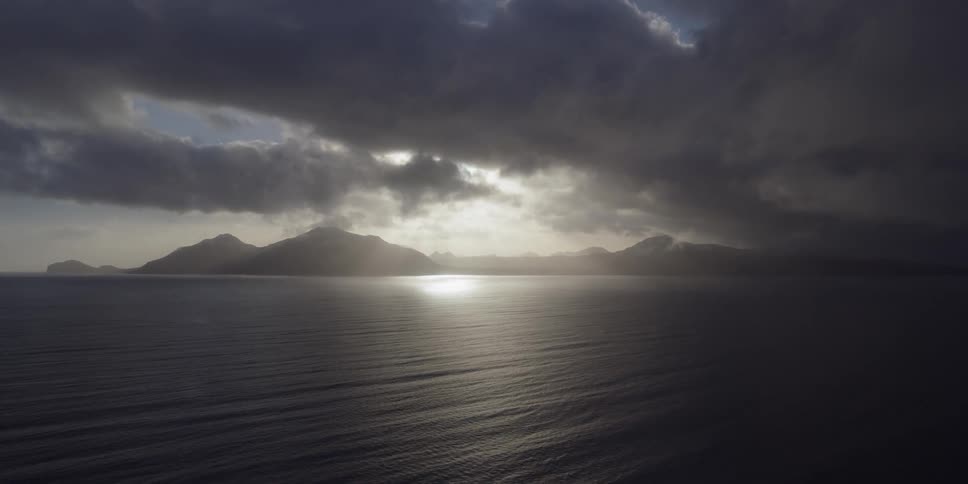 The sun is casting a spot of light through storm clouds onto the ocean
