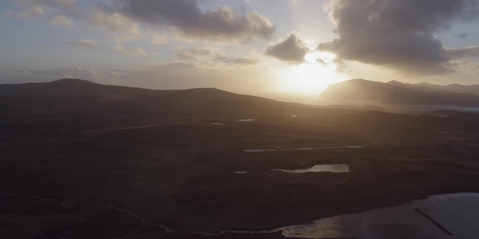 The sun is rising over a mountainous coastal region