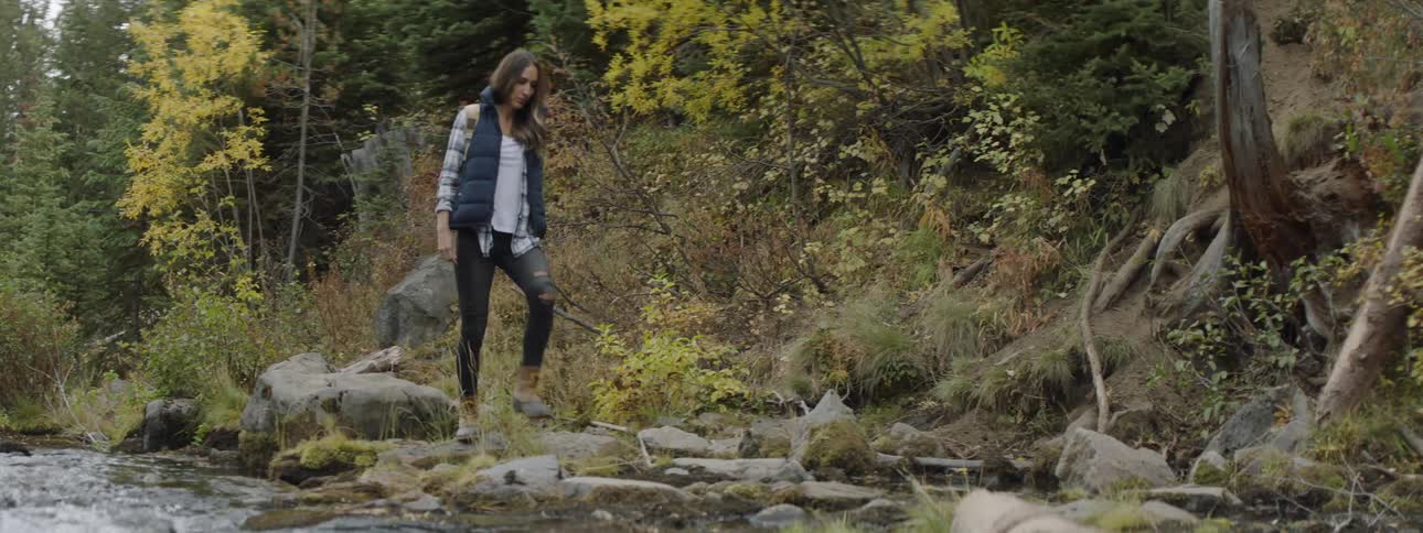 A woman walks on rocks on the river shore