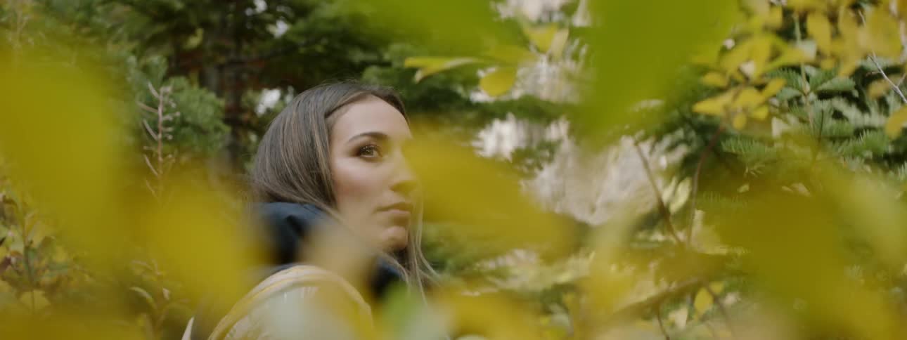 Woman walking through a forest and pausing to look behind her for a moment while wearing a backpack