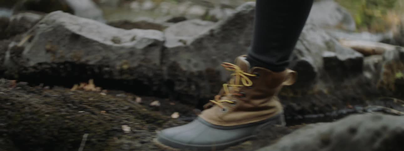 Person wearing boots steps over large rocks in  nature