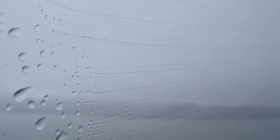 Raindrops pushed by wind across a vehicle window
