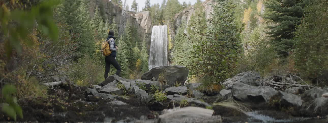 A woman is standing and watching a waterfall in a natural setting during the day